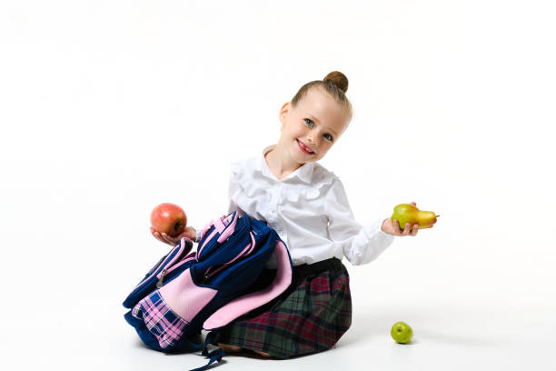 Beautiful schoolgirl is holding book and apple,she likes to have healthy snack  while she is learning.
