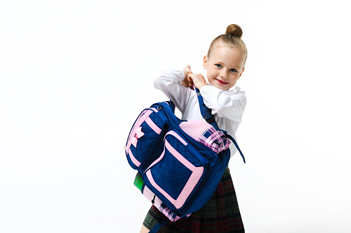 Cute girl in a school uniform with a big and heavy backpack on a white background