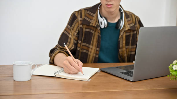 istock A hipster young Asian male college student using laptop and taking notes on his book. cropped 1421488504