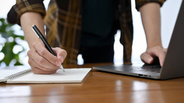 istock A professional male office worker in flannel shirt working at his desk, taking notes and using laptop 1421488557
