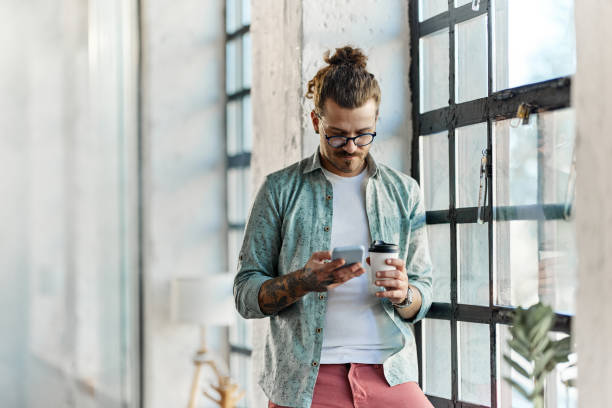 istock Male freelancer using cell phone on coffee break by the window. 1421499596