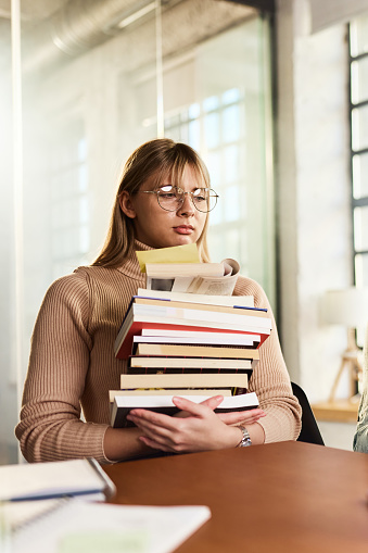 Young student feeling bored holding large group of books.