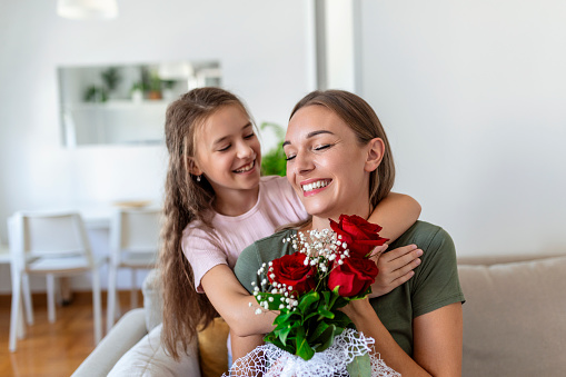 I love my you mom! Attractive young woman with little cute girl are spending time together at home, thanking for handmade card with love symbol and flowers. Happy family concept. Mother's day.