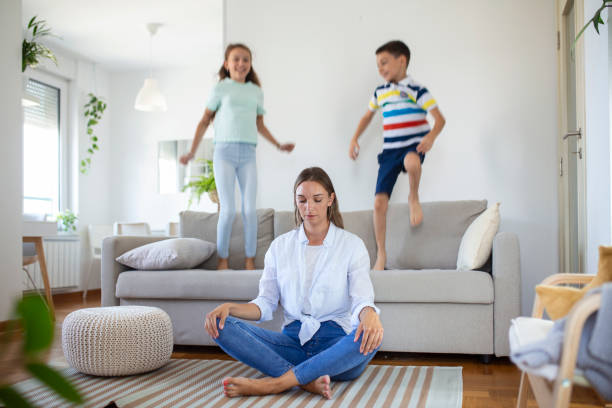 istock mother with closed eyes meditating in lotus pose on floor trying to save inner harmony while excited children jumping on sofa and screaming in light spacious living roo 1421502315