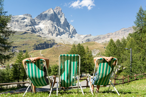 Couple and their little girl relaxing in deck chairs in a garden with views at the iconic Matterhorn.