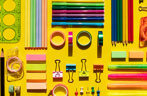 Office and school supplies arranged on yellow background