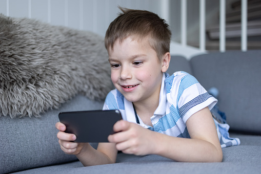 Happy boy lying down on the sofa in the living room and looking at mobile phone