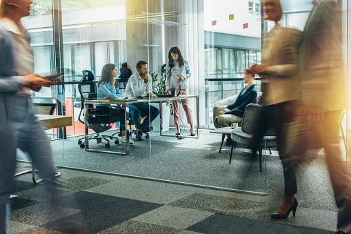 Blurred motion of businesspeople on the go and project team members discussing ideas in a conference room.