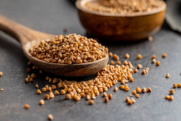 istock Uncooked buckwheat grain in wooden spoon on black table. 1421513372