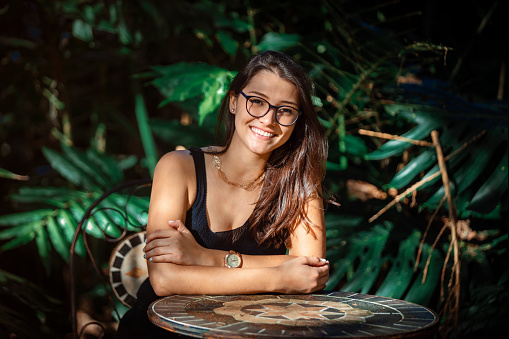 beautiful young Latina woman sitting at a table with jungle type background. High quality photo