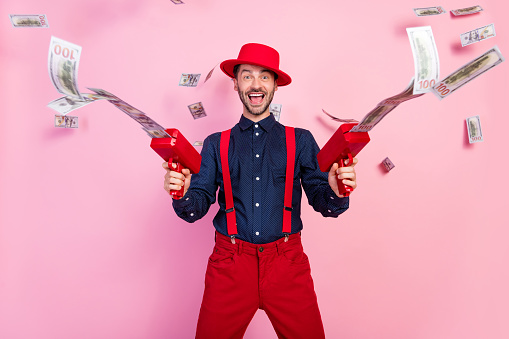 Photo of positive excited gun hold use money gun flying banknotes isolated on pink color background.