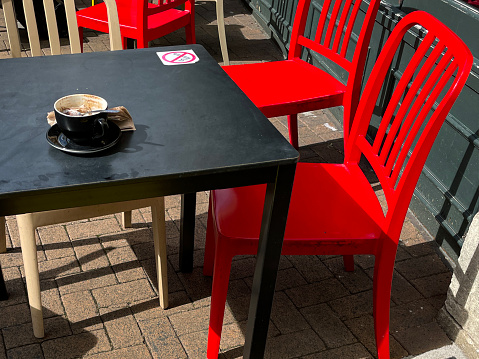 Stock photo showing a wooden table and red chairs pictured outside a pavement cafe.