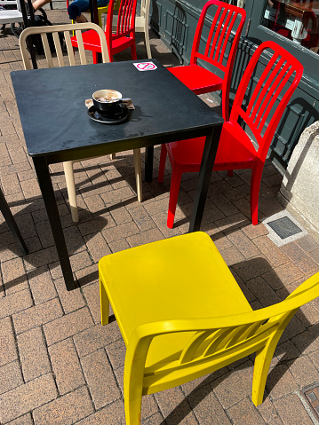 Stock photo showing a wooden table with red and yellow chairs pictured outside a pavement cafe.