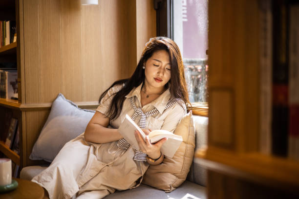 istock Women reading book sitting on windowsill 1421520761