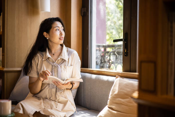istock Woman sitting on sofa reading a book by window 1421520762