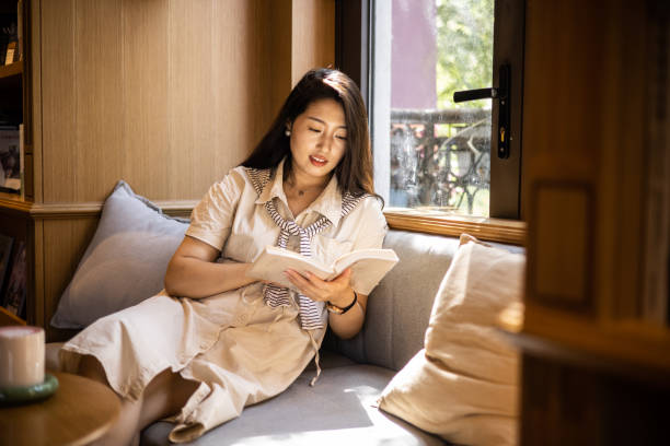 istock Women reading book sitting on windowsill 1421520916