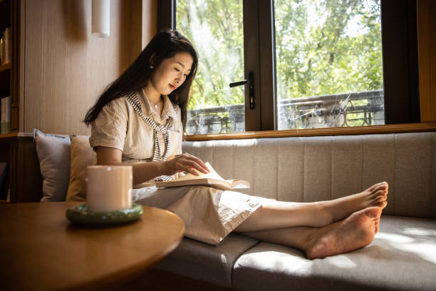 istock Women reading book sitting on windowsill 1421521016