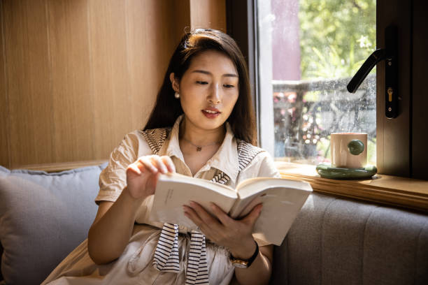 istock Women reading book sitting on windowsill 1421521073