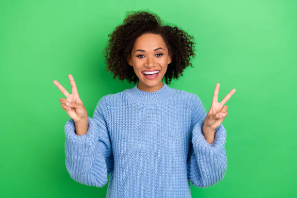 istock Photo of cheerful good mood  woman with perming coiffure dressed blue oversize pullover showing v-sign isolated on green color background 1421521222