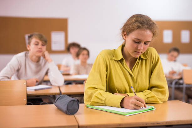 istock Teenage students studying in classroom with teacher, writing lectures in workbooks 1421522723