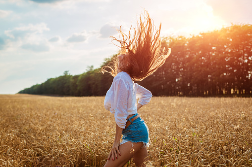 Beautiful young woman in wheat field. Cute brunette girl of Caucasian appearance in casual clothes is resting, happy in a ripe wheat field on a sunny day, dancing in the sun