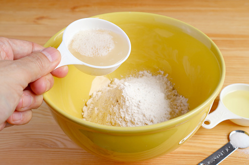 Man's hand pouring yeast with water into the bowl of flour