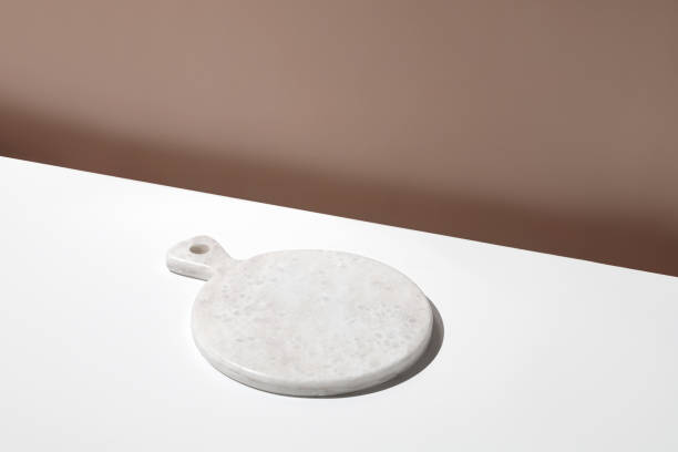 istock White empty marble board on white table. Blank, still life scene, beige wall, background with plate. 1421527663