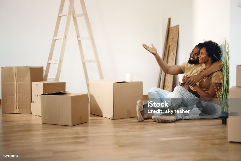 Happy black couple making plans after moving into a new apartment. Happy African American couple making decoration plans while taking a break from unpacking their belongings in a new home. Copy space. Moving House Stock Photo