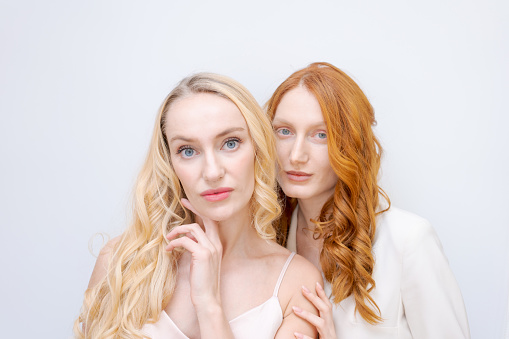 Portrait two cheerful blonde and redhead women in summer wear smiling, posing in clothes, shoulder-length photo close-up isolated on a light background