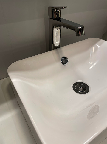 Stock photo showing close-up view of modern, freestanding white sink and chrome, single lever, monobloc tap over black vanity unit with cream counter top.