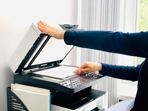 A person uses a copier to copy documents or digitally scan.