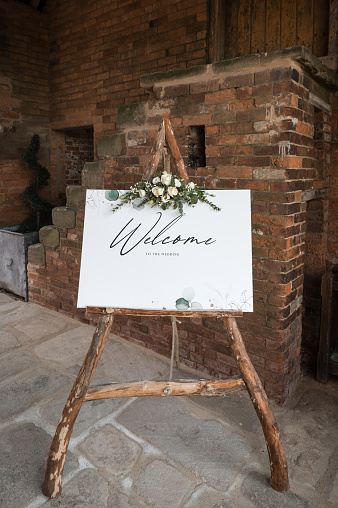 Welcome sign to wedding, wooden frame natural wood with flowers bouquet floral display.  Standing outside wedding venue to welcome guests.