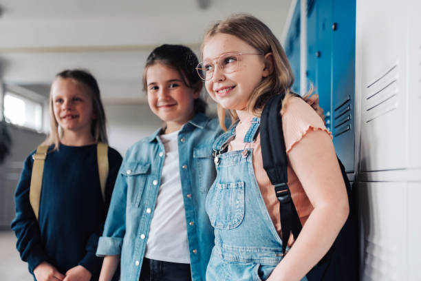 three elementary school girls leaning at locker in school stock photo