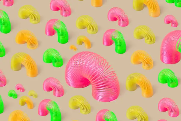 Rainbow plastic multicolored spiral toys or slinky on beige background. Minimalism. Creative seamless pattern