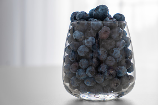 Blueberry in the glass standing on the white table. Healthy snack