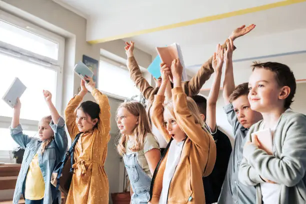 high angle view on group of school children standing in a row and raising up hands with work books