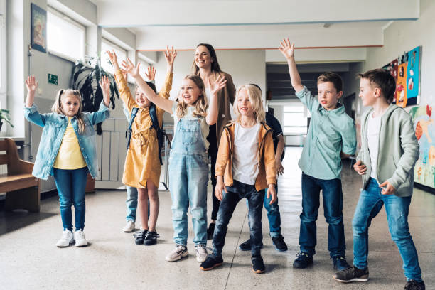 istock group of elementary school children with teacher raising up hands together 1421537230