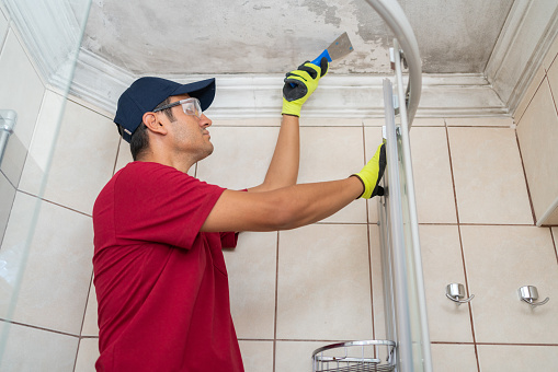 Male Worker Scraping Bathroom Ceiling With Spatula
