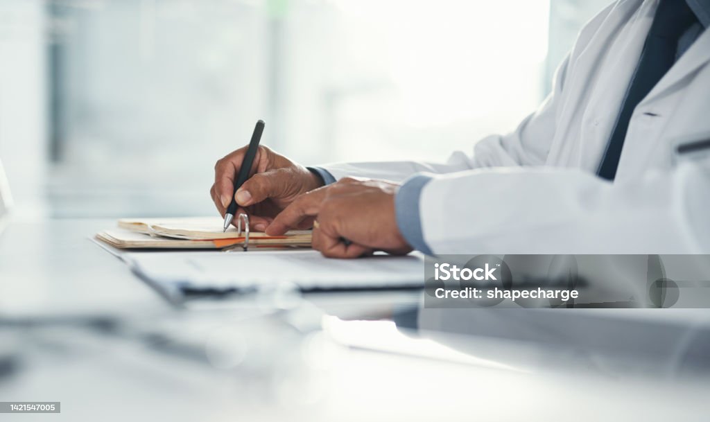 Doctor hands writing on paper or document at a desk in the hospital. Healthcare professional drafting a medical insurance letter, legal paperwork or form. A GP filing a document in a clinic office Doctor Stock Photo