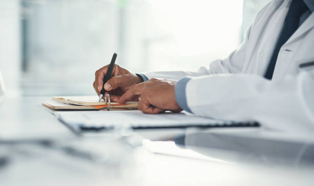 Doctor hands writing on paper or document at a desk in the hospital. Healthcare professional drafting a medical insurance letter, legal paperwork or form. A GP filing a document in a clinic office stock photo