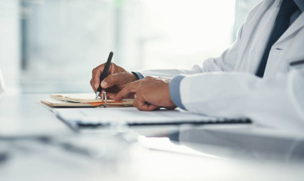 o médico escreve em papel ou documento em uma mesa no hospital. profissional de saúde elaborando uma carta de seguro médico, papelada legal ou formulário. um gp arquivando um documento em um consultório de clínica - form filling - fotografias e filmes do acervo