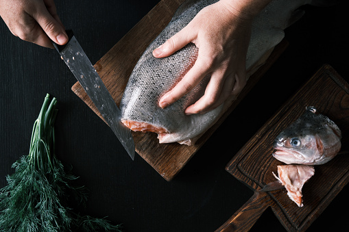 Unrecognizable person is cutting salmon in domestic kitchen