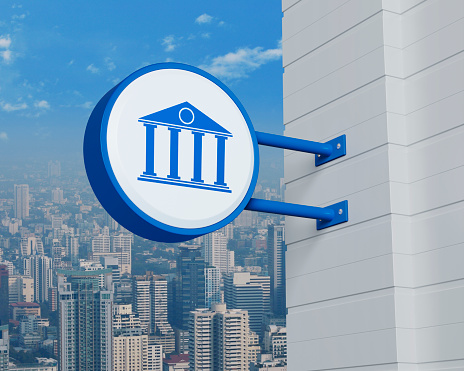 Bank icon on hanging blue rounded signboard over modern city tower, office building and skyscraper, Business banking online service concept, 3D rendering