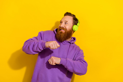 Photo of charming sweet guy dressed purple sweater headphones dancing looking empty space isolated yellow color background.