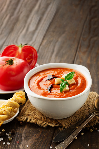 Autumn Homemade Tomato Soup with Bread Sticks, tomatoes, red pepper, herbs and spices on dark rustic wooden background, copy space.