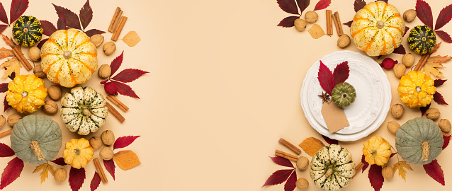 Autumn holiday Thanksgiving table place setting. Pumpkins, porcelain white plate, dry maple leaves, spice and apple on beige pastel background. Flat lay, top view, copy space.