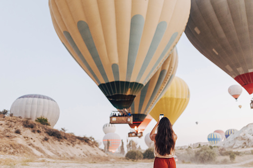 Young woman tourist taking a photo on smartphone of hot air balloons in Cappadocia
