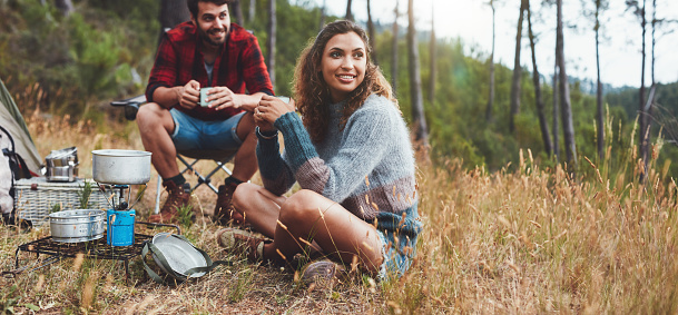 Cheerful young couple having some coffee while camping in nature. Happy young couple having a good time on a camping holiday.
