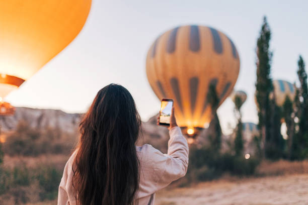 une jeune touriste prenant une photo sur smartphone de montgolfières en cappadoce - ballooning festival photos et images de collection