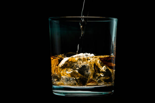 Pouring Whiskey A close-up shot of a whiskey glass filled with ice on a black background. Whiskey is being poured into the glass from above. glass of bourbon stock pictures, royalty-free photos & images